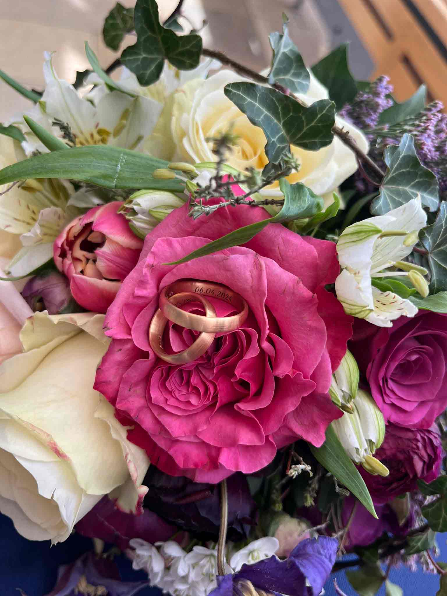 Brautstruß mit Rosen, in der Mitte liegen Eheringe aus FAIRMINED ECO GOLD